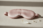 Soft pink natural silk sleep mask displayed on a clean light beige background. Soft diffused lighting highlighting the silky shine. Minimal, elegant composition. Luxury product photography, high resolution.